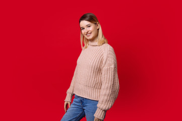 Portrait of cheerful young blonde woman looking at camera, standing over red background in studio