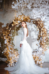 Fashion portrait of beautiful young woman in a gorgeous wedding dress, posing in a fantasy interior with white winter tree © cherry_d