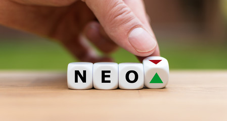 Hand is turning a dice and changes the direction of an arrow symbolizing that the value of the crypto currency NEO is going up (or vice versa)