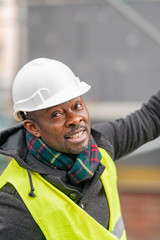 African American engineer wearing yellow protective workwear looking upwards among scaffolding