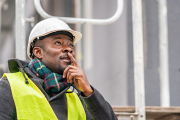 African American engineer wearing yellow protective workwear looking upwards among scaffolding