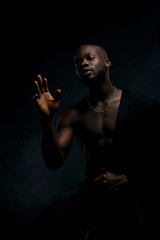 Dark key portrait of sexy musician man topless, with jacket on one shoulder. Studio shot, black background