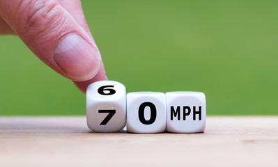 Hand is turning a dice and changes the expression "70 MPH" to "60 MPH" as symbol to reduce the speed limit from 70 to 60 miles per hour