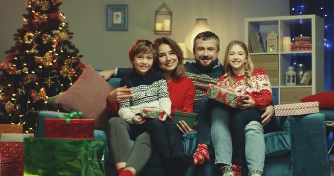 Caucasian cute kids, sister and brother, sitting on the laps of their mother and father smiling to the camera in the x-mas decoration of their home.