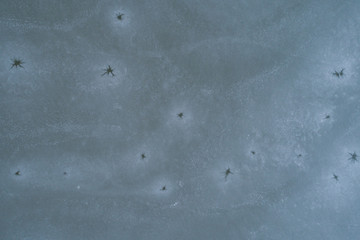 Aerial view on frozen water surface with cracks and ice holes. Ice texture.