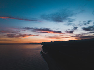 Fototapeta na wymiar Bellissimo cielo al tramonto infuocato con nuvole arancione e rosso in riva all'oceano calmo. Vista aerea