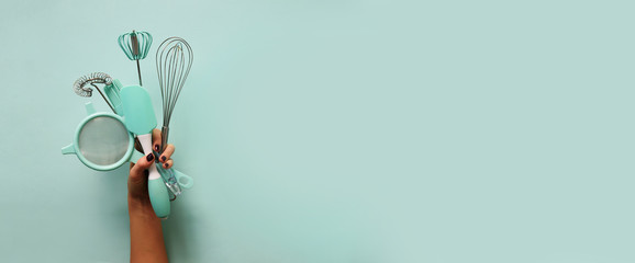 Baking flat lay. Female hands holding kitchen tools, sieve, rolling pin, spatula and bruch on pastel blue background. Banner with copy space. Top view