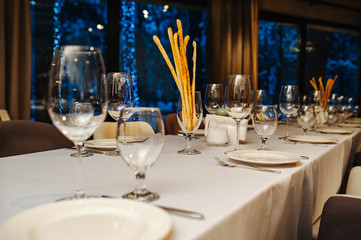 Tableware for new year banquet. Glasses, plates, fork, knife,served for dinner in restaurant with cozy interior. Wedding decorations and items for food, arranged by the catering service on large table
