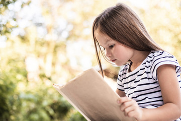 Obraz premium Little girl mindfully reading book in park