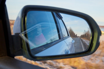 Side mirror of the car and the reflection of the road in it. Autumn landscape