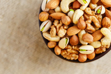 Mix of different nuts in a wooden cup against the background of fabric from burlap. Nuts as structure and background, macro. Top view.