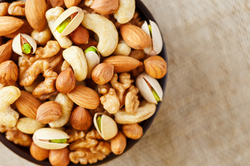 Mix of different nuts in a wooden cup against the background of fabric from burlap. Nuts as structure and background, macro. Top view.