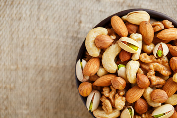 Mix of different nuts in a wooden cup against the background of fabric from burlap. Nuts as structure and background, macro. Top view.