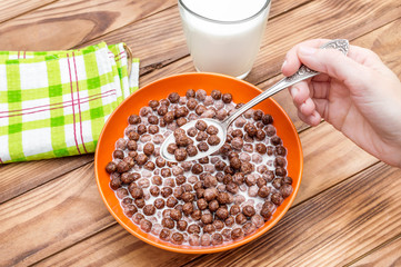 Woman eating chocolate corn balls with milk at the table.