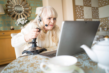 Senior woman plays video games with joystick on a laptop