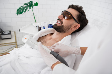 Happy man wearing laser safety goggles during hair removal procedure - obrazy, fototapety, plakaty