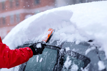Transportation, winter, weather, people and vehicle concept - man cleaning snow from car with brush.