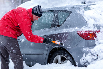 man cleaning car windshield of snow winter scraper.