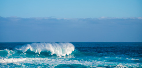 Single perfect wave in blue deep dangerous ocean - perfect barrel for brave surfers - coast in background for touristic scenic place - enjoy the beauty of the world and the feeling of the sea