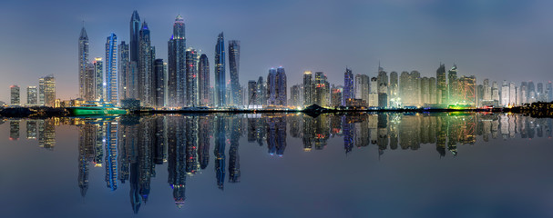 Die beleuchtete Skyline der Dubai Marina bei Nacht mit Reflektionen in der Bucht