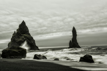 A beach with volcanic sand and rocks sticking out of the water. Black and white photo. Stormy Ocean. Iceland. Beach Vic. 
