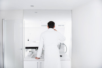 Man in bathrobe standing in front of the mirror in bathroom - obrazy, fototapety, plakaty