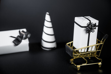 White Christmas tree and gift in shop cart isolated on black background.