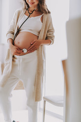 Relaxed young mom standing and listening baby heartbeat