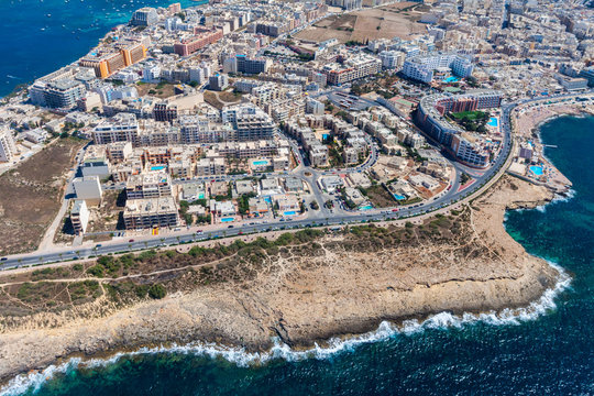 Seaside cliffs, colourful houses and streets of Qawra town in St. Paul's Bay area in the Northern Region, Malta. Popular tourist resort between Bugibba and Salina. Aerial view. Malta island from above