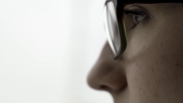 Extreme close up for young female face portrait in profile in black glasses on fuzzy, white background. Beautiful woman with her face in profile and short, dark hair.