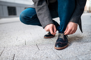 Businessman tying shoelace outdoors, close-up.
