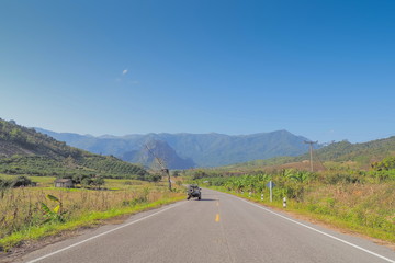 Scenic highway route 1148, view of a 4x4 truck on the road around with green meadow, mountain and blue sky background, Tham Sakoen National Park, Nan, northern of Thailand.