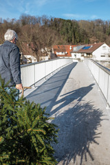 Mann mit Weihnachtsbaum in Leiterwagen geht über eine Brücke und wirft Schatten