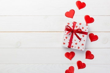 Valentine or other holiday handmade present in paper with red hearts and gifts box in holiday wrapper. Present box gift on white wooden table top view with copy space, empty space for design