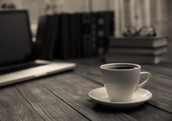 A cup of coffee in the workplace on a wooden table.