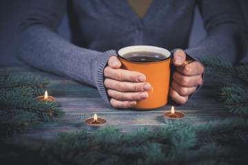 Woman holds a cup of hot tea among the fir branches and candle.