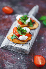 Italian bruschetta with tomatoes, mozzarella and herbs on a wooden board on a dark background