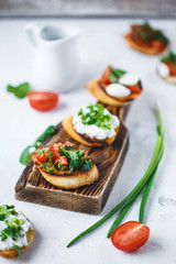 several types of italian bruschetta with tomatoes, mozzarella and herbs on a wooden board on a light background