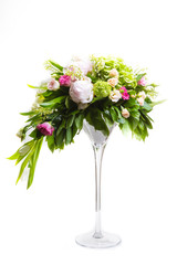 A large number of yety, a large lush bouquet of snowdrop, rose, bell and peony with greens in a large long stylish transparent vase on the leg on a white isolate background