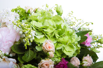 A large number of yety, a large lush bouquet of snowdrop, rose, bell and peony with greens in a large long stylish transparent vase on the leg on a white isolate background