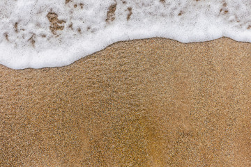 Top view of surface of clean golden sand at sea beach and white foamy wave. Horizontal color photography.