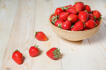 Fresh strawberries in a bowl on wooden table with low key scene.