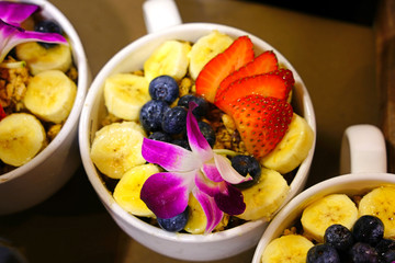 Acai bowl with granola, banana and fresh berries decorated with an orchid flower