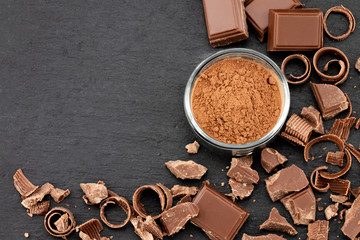 Broken chocolate pieces and cocoa powder on a dark background. Top view with copyspace for your text