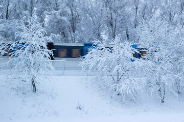 Wintery landscape with fluffy snow and commuter train speeding by, in Stockholm, Sweden.