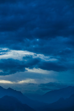 Amazing night landscape of calm clouds, blue sky and silhouettes of high mountains. Vertical color photography.