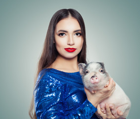 Beautiful brunette woman in blue glitter dress holding little pig