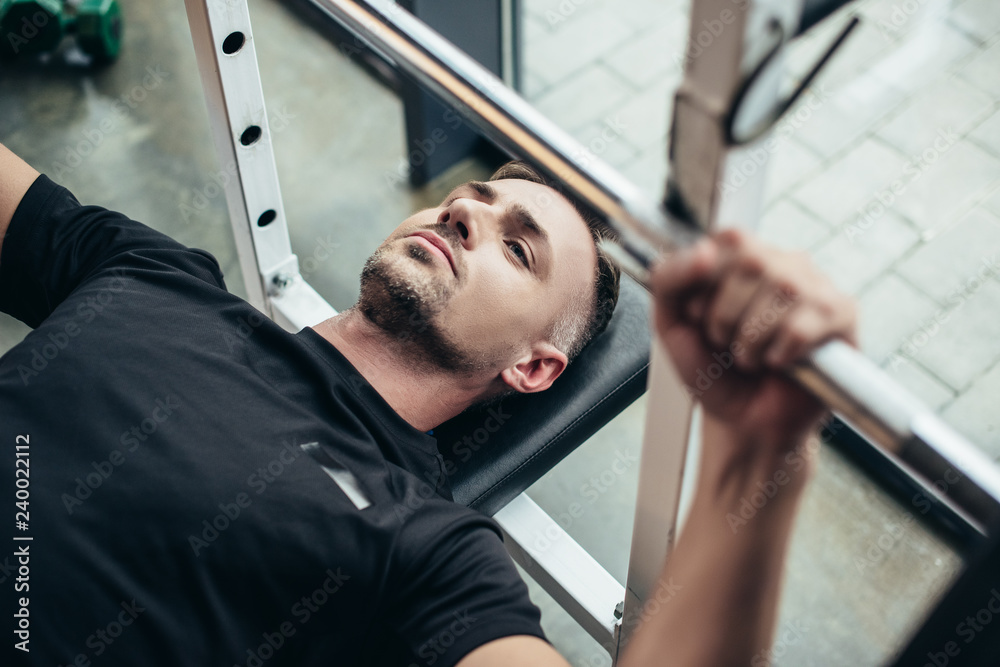 Wall mural selective focus of sportsman lifting barbell while lying on bench in gym