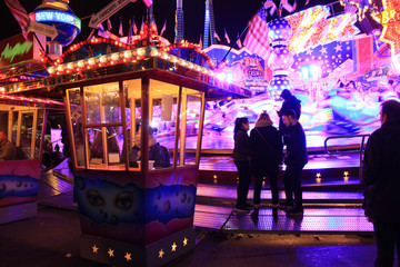 Fototapeta premium Two women and a guy in front of a thrill ride. Night amusement group of three persons. 