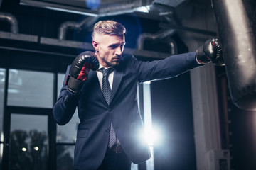 handsome businessman in suit boxing with punching bag in gym